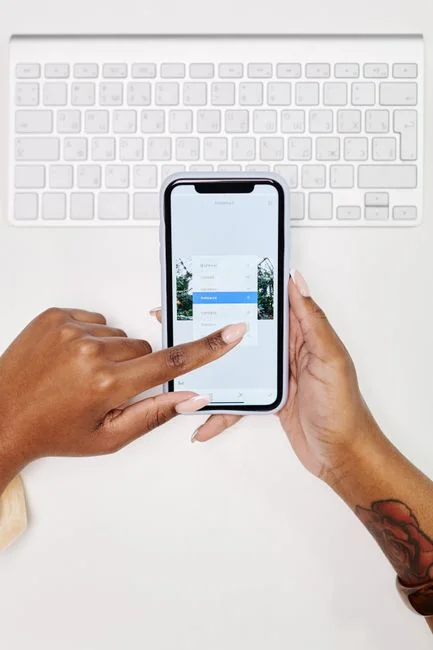 Hands using smartphone beside laptop with stock charts, showcasing digital trading.