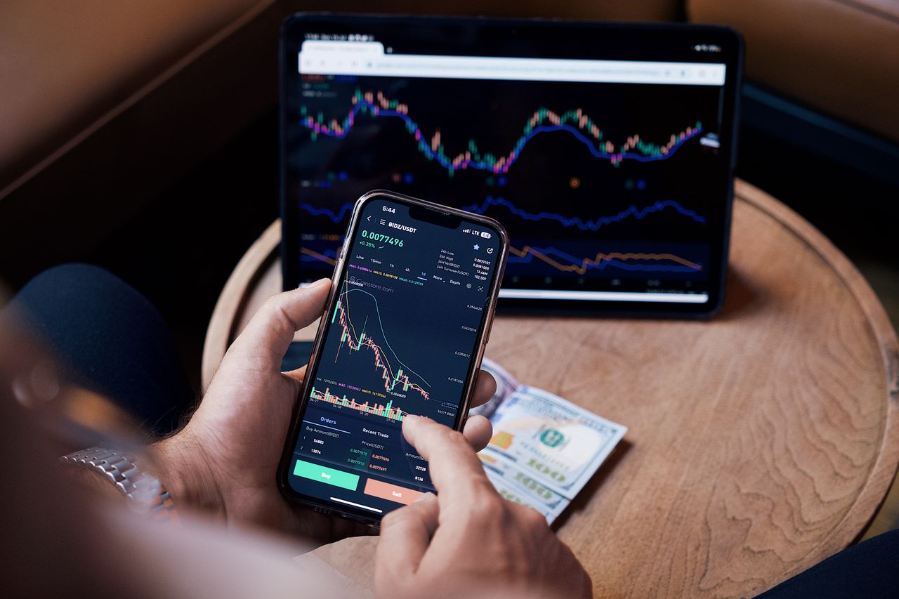Gros plan d'une personne effectuant des transactions boursières à l'aide d'un smartphone et d'une tablette.